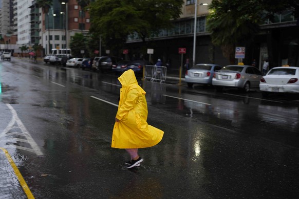 29.06.2022, Venezuela, Caracas: Eine Frau spaziert im Regen und tr�gt einen gelben Regenmantel. Foto: Ariana Cubillos/AP/dpa +++ dpa-Bildfunk +++