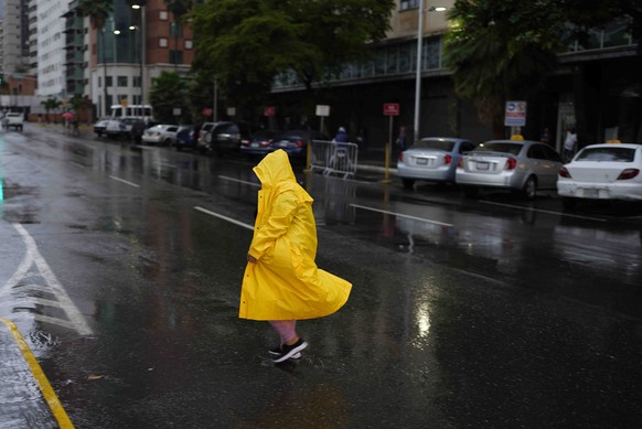 29.06.2022, Venezuela, Caracas: Eine Frau spaziert im Regen und tr�gt einen gelben Regenmantel. Foto: Ariana Cubillos/AP/dpa +++ dpa-Bildfunk +++