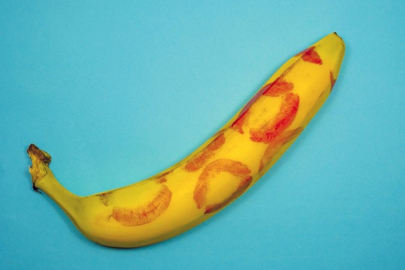 Red lipstick on a yellow banana on a blue background. Oral sex concept.