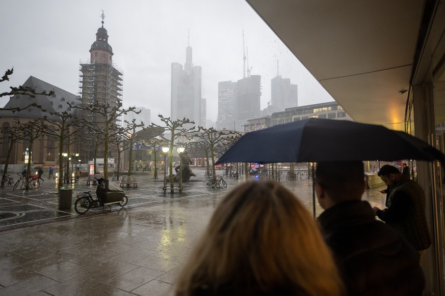 13.03.2023, Hessen, Frankfurt/Main: Menschen stehen während eines starken Regengusses auf der Frankfurter Einkaufsstraße Zeil unter dem Vordach eines Geschäfts. Zum Wochenstart kommt es in Hessen zu t ...