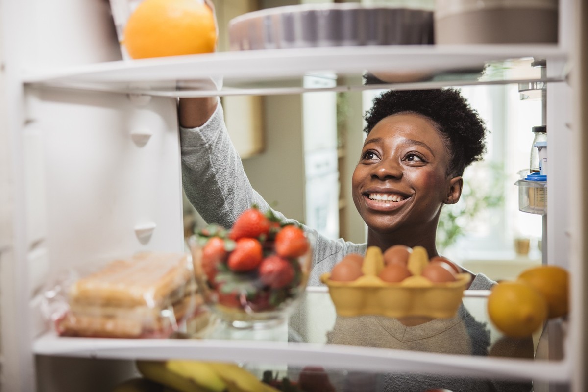 oman taking food from fridge full of groceries.