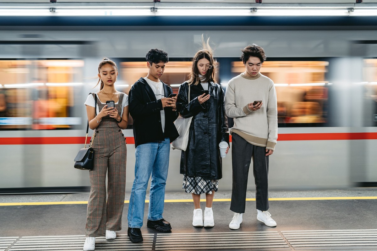 Group of Asian teenagers using phones in subway station. Social issues concept.