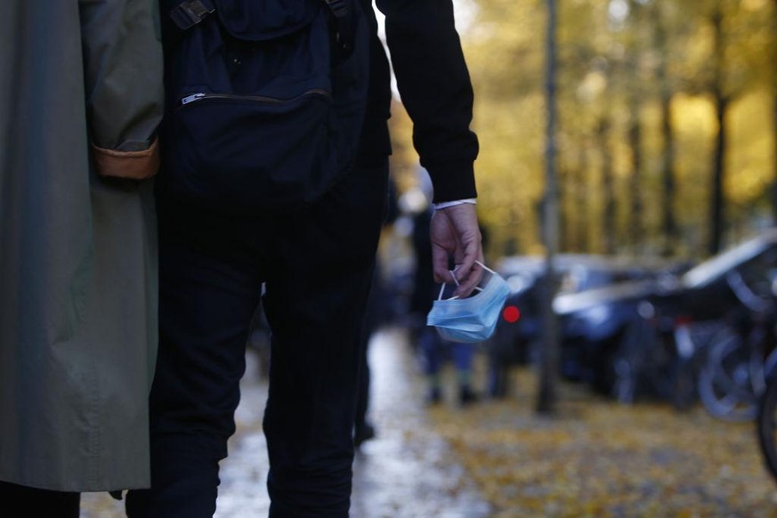 BERLIN, GERMANY - OCTOBER 24: People carry a protective face masks in the hand as they walk along Bergmanstrasse, one of the main shopping street in Kreuzberg district, on the first day that a require ...