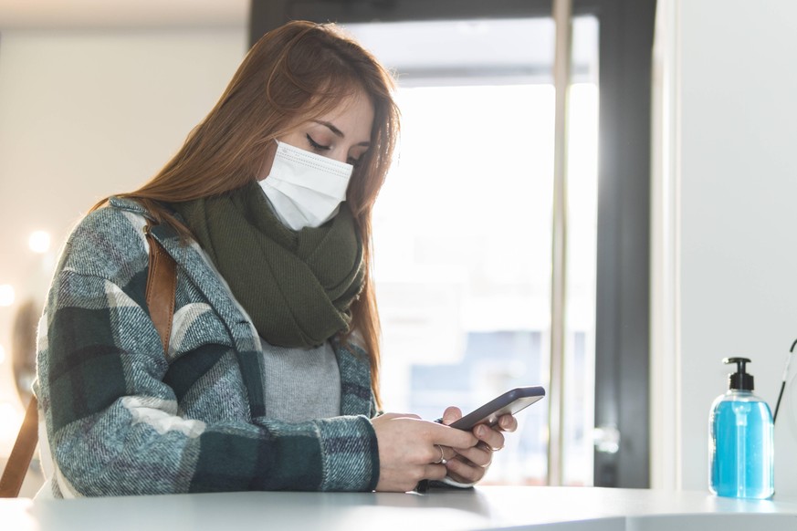 Portrait of young woman wearing protective face mask waiting in beauty salon lobby with smart phone in hands model released Symbolfoto property released JAQF00398
