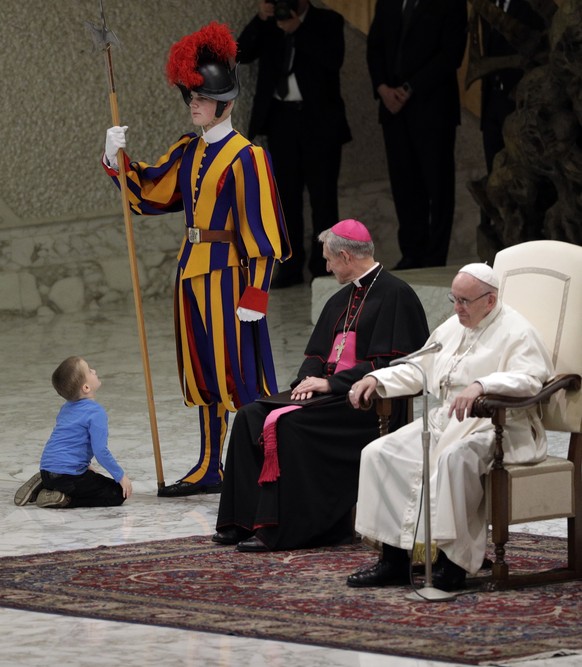 A child looks up at a Swiss guard after getting up to the area where Pope Francis and Archbishop George Gaenswein are sitting, during the pontiff&#039; weekly general audience in the Paul VI Hall at t ...