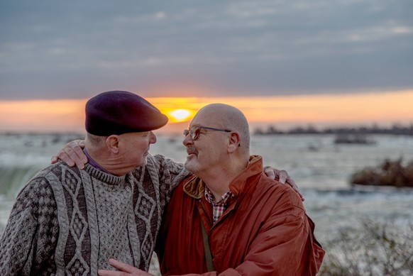 Homosexual married Caucasian men in their late 60&#039;s still in love and playful at Niagara Falls, Ontario, Canada. The couple is touring the Falls at sunrise.