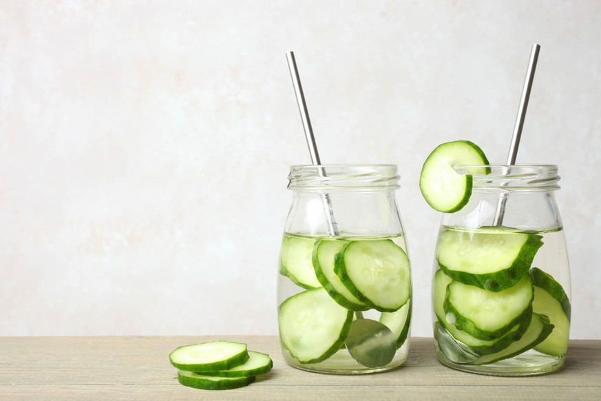 Two Jar of refreshing dietary water with cucumber and with metal straws on wooden table on neutral background. Concept detox drink. Copy space.