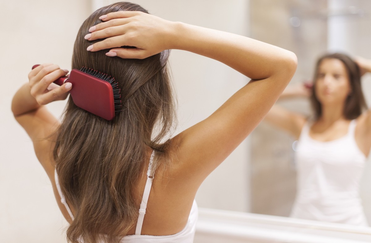 Young woman brushing healthy hair in front of a mirror