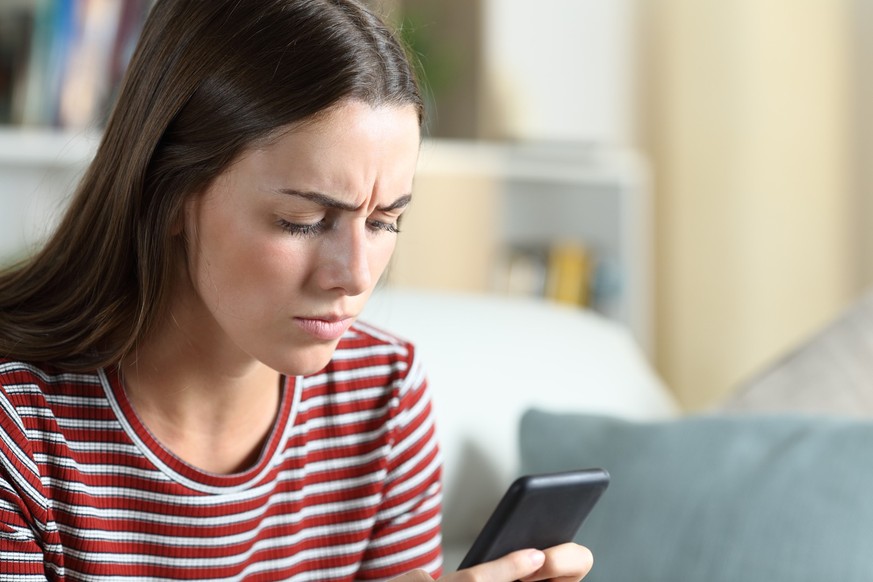 Annoyed woman checking smart phone at home