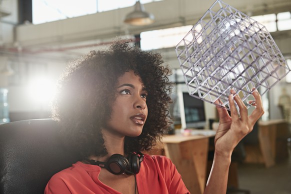 Shot of a young female designer looking thoughtfully at the cube model she&#039;s holding