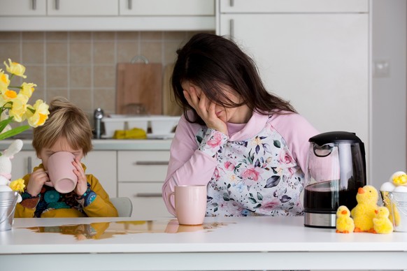 Tired mother, trying to pour coffee in the morning. Woman lying on kitchen table after sleepless night, trying to drink coffee