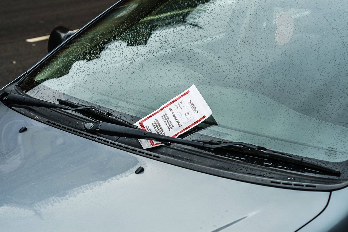 An einem Auto ist zwischen Scheibenwischer und Windschutzscheibe ein Parkkn�llchen ferstgeklemmt. Edinburgh, Highland, Schottland. Strafzettel am Scheibenwischer *** to a Car is between Wipers and Win ...