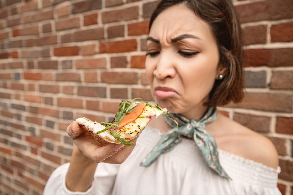 A girl with a sad face looks at a delicious piece of high-calorie pizza. Diet and digestive problems as well as spoiled and tasteless food