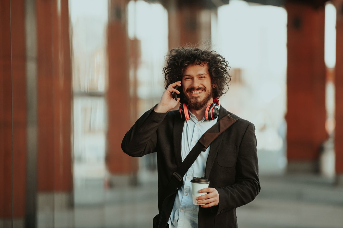 Happy young American holding a coffee. With headphones. Student boy., Happy student with afro haircut walking on campus while wearing his manbag and his headphones. model released