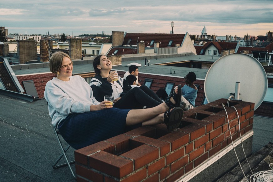 IMAGO Creative, Lifestyle, Leben in einer Wohngemeinschaft, WG IMAGO Kreativ: Urbane Kultur - Sommer auf den Dächern Smiling female talking to friend while enjoying drink on building terrace Germany,  ...