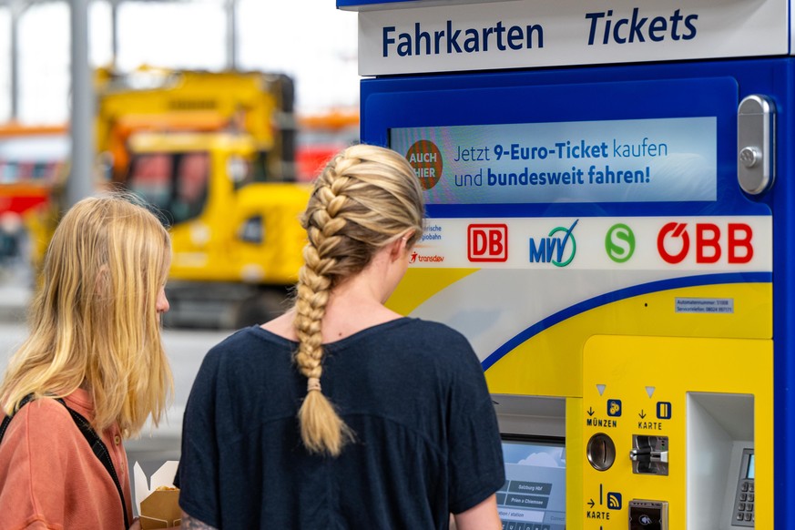 Zwei junge Frauen stehen am Hauptbahnhof in München an einem Fahrkartenautomaten auf dem Werbung für das 9-Euro-Ticket zu sehen ist.