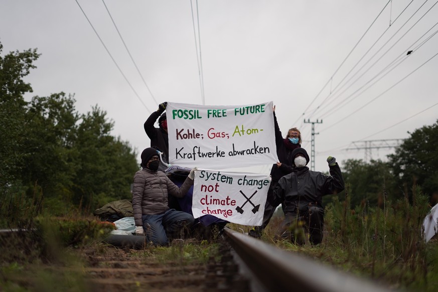 19.09.2022, Brandenburg, Jänschwalde: Klimaaktivisten der Gruppe &quot;unfreiwillige Feuerwehr&quot; blockieren Gleise am Kohlekraftwerk Jänschwalde und posieren mit Plakaten &quot;Fossil free future& ...