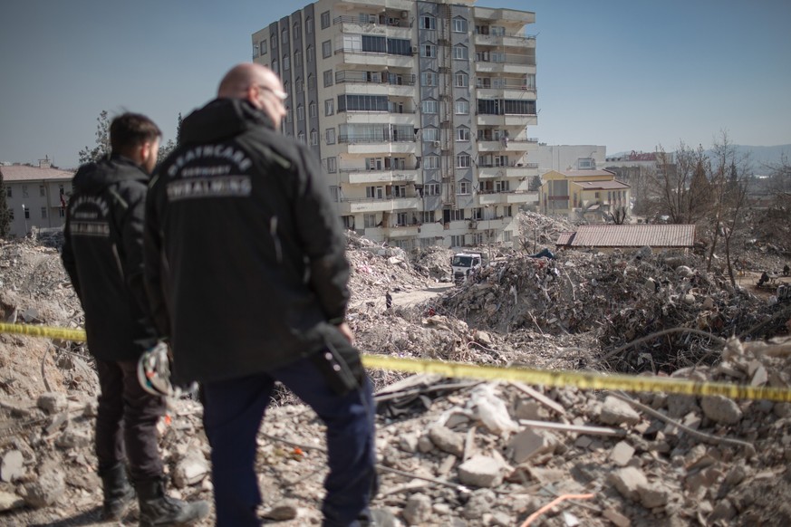 PRODUKTION - 18.02.2023, Türkei, Kharamanmaras: Rene Stawinski (r), Bestatter und Leiter des Teams der ehrenamtlichen Organisation «Deathcare» aus Deutschland, inspiziert ein eingestürztes Gebäude im  ...