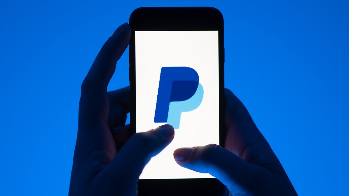 ARCHIV - 12.05.2022, Sachsen, Dresden: ILLUSTRATION - Eine Frau hält ein Smartphone mit dem Logo des Bezahldienstes Paypal. (gestellte Szene) Das Bundeskartellamt hat ein Verfahren gegen den Online-Be ...
