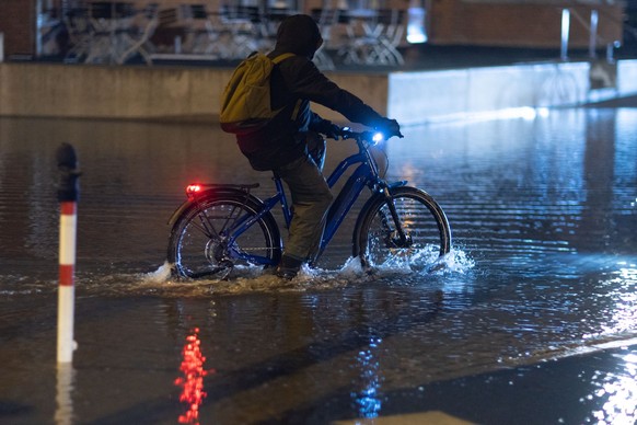 20.10.2023, Mecklenburg-Vorpommern, Wismar: Ein Radfahrer fährt durch das Hochwasser am Stadthafen. Wegen einer erwarteten Sturmflut an der Ostseeküste sind Uferbereiche in der Nähe des Hafens bereits ...