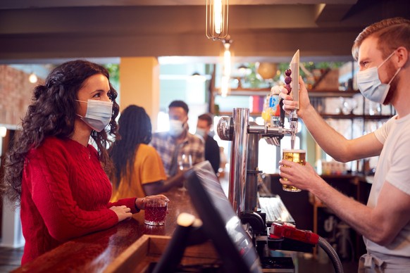 Male Bartender Wearing Face Mask Serving Female Customer With Drink During Health Pandemic