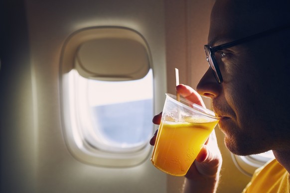 Young passenger enjoying dring during flight. Man holding cocktail against airplane window.