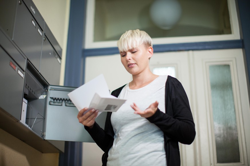 ILLUSTRATION - Eine Frau oeffnet am 07.09.2016 in einem Wohnhaus in Hamburg am Briefkasten einen Briefumschlag (gestellte Szene). Foto: Christin Klose || Modellfreigabe vorhanden