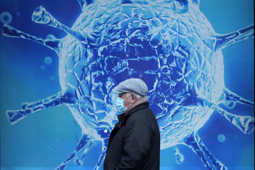 OLDHAM, UNITED KINGDOM - NOVEMBER 24: A man wearing a protective face mask walks past an illustration of a virus outside Oldham Regional Science Centre on November 24, 2020 in Oldham, United Kingdom.  ...