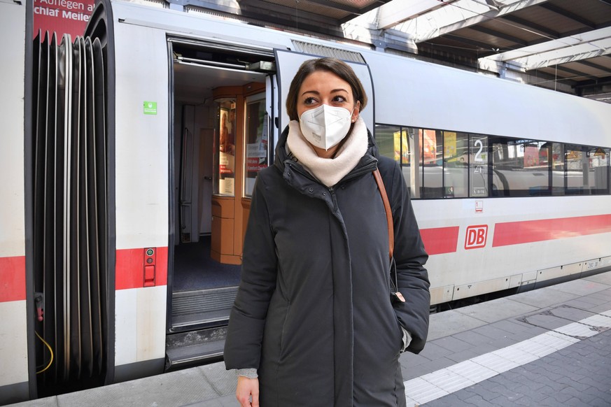 FOTOMONTAGE: Deutsche Bahn prueft Einfuehrung einer FFP2 Maskenpflicht. Junge Frau mit FFP2 Maske, Oeffentliches Leben in Zeiten der Coronavirus Pandemie. Geoeffnete Tuer an einem Waggon,Wagen von ein ...