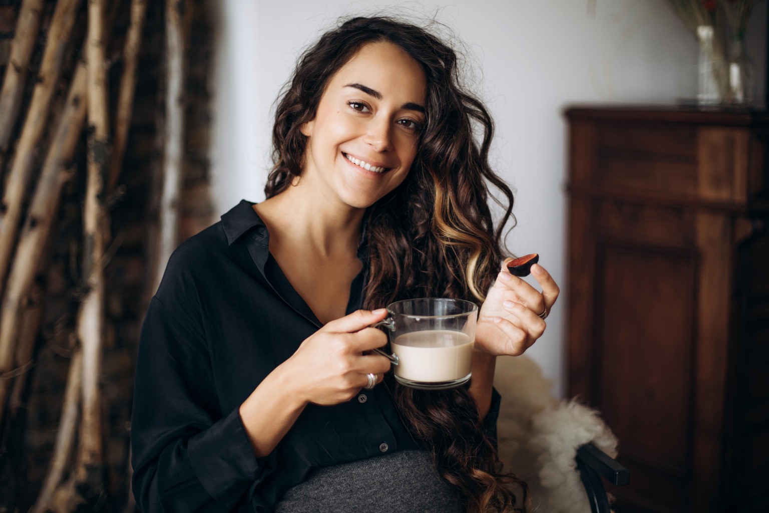 Portrait of a beautiful pregnant woman with a cup of coffee and figs in hands at home.