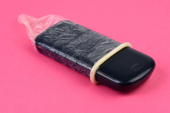 Mobile phone is inside a condom as a symbol for safe sex on phone. Isolated on pink background, studio shot. Letters on the phone are cleaned.