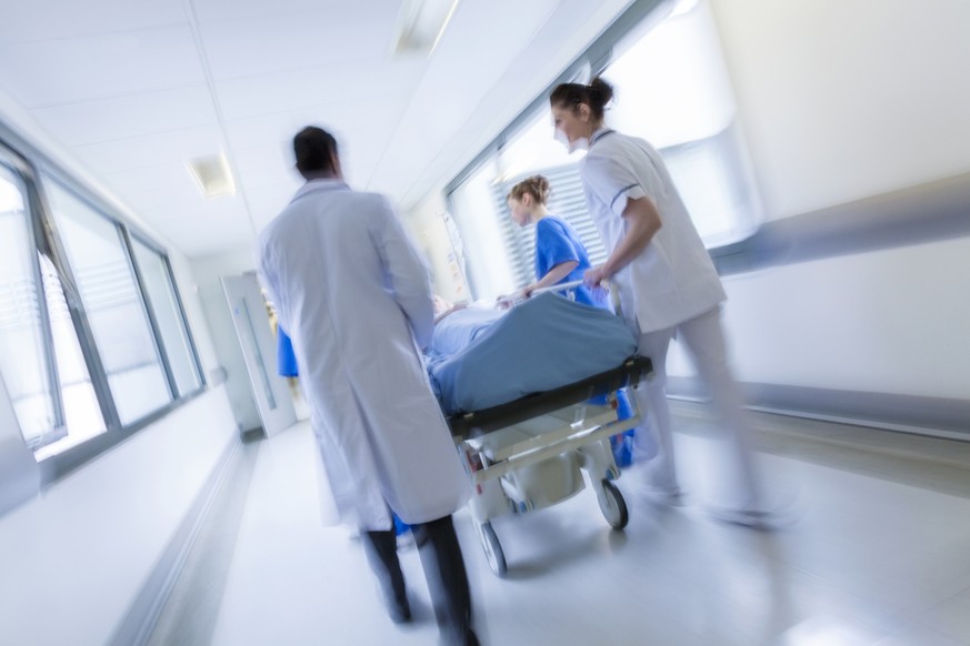 A motion blurred photograph of a patient on stretcher or gurney being pushed at speed through a hospital corridor by doctors &amp; nurses to an emergency room