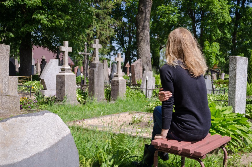 Sorrow woman shrinked near father husband tomb in cemetery.