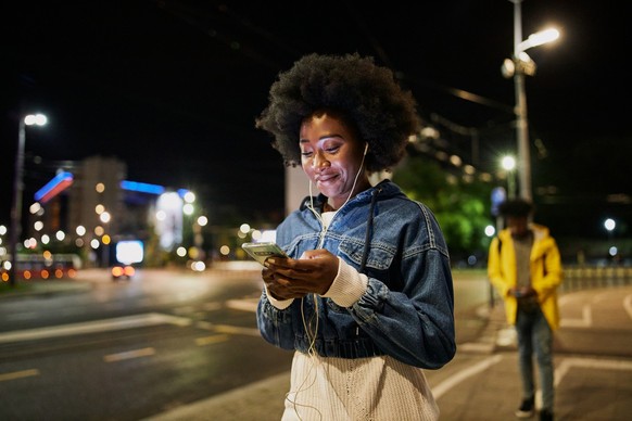 Young adult African American woman text messaging on her mobile phone while being followed by a man