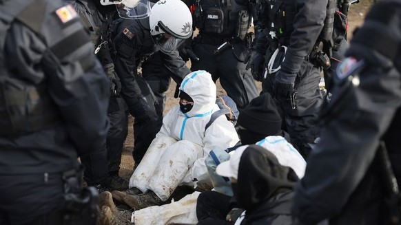 10.01.2023, Nordrhein-Westfalen, Erkelenz: Polizeibeamte entfernen einen Klimaschutzaktivisten aus einer Straßenblockade am Rand der Ortschaft Lützerath. Lützerath soll zur Erweiterung des Braunkohlet ...