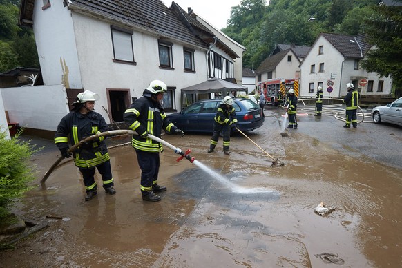 Feuerwehrleute säubern einen Gehweg und eine Straße vom Schlamm in Isenburg (Rheinland-Pfalz): Nach einem heftigen Gewitter sind Straßen und Keller überflutet.