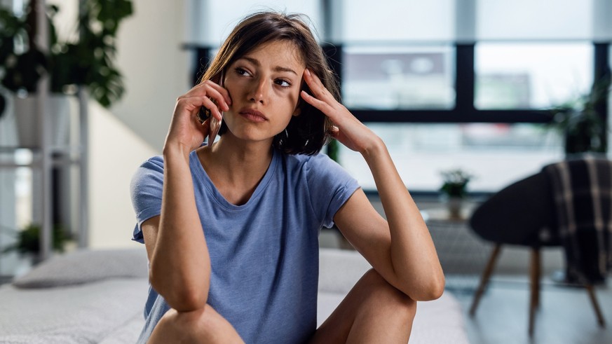 Young sad woman communicating over mobile phone and looking away while thinking of something.