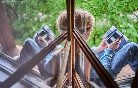 ARCHIV - 28.05.2022, Berlin: Ein Junge sitzt am Fenster und schaut auf sein Handy. Die Mehrheit der Eltern in Deutschland hat einer Umfrage zufolge wegen der hohen Mediennutzung ihrer Kinder ein schle ...