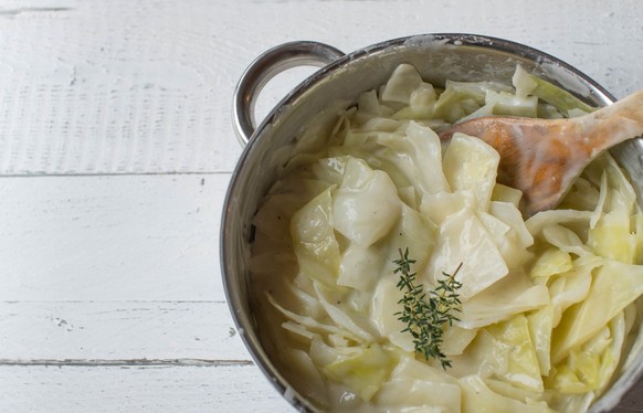 Traditional fresh and homemade cooked chopped white cabbage with delicious bechamel or white sauce. Served hot and ready to eat in a pot with wooden spoon isolated on white background. Top view, side  ...