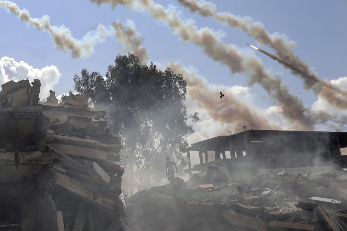 19.10.2023, Palästinensische Gebiete, Gaza-Stadt: Raketen aus dem Gazastreifen werden über zerstörte Gebäude hinweg auf Israel abgefeuert. Foto: Mohammed Dahman/AP +++ dpa-Bildfunk +++