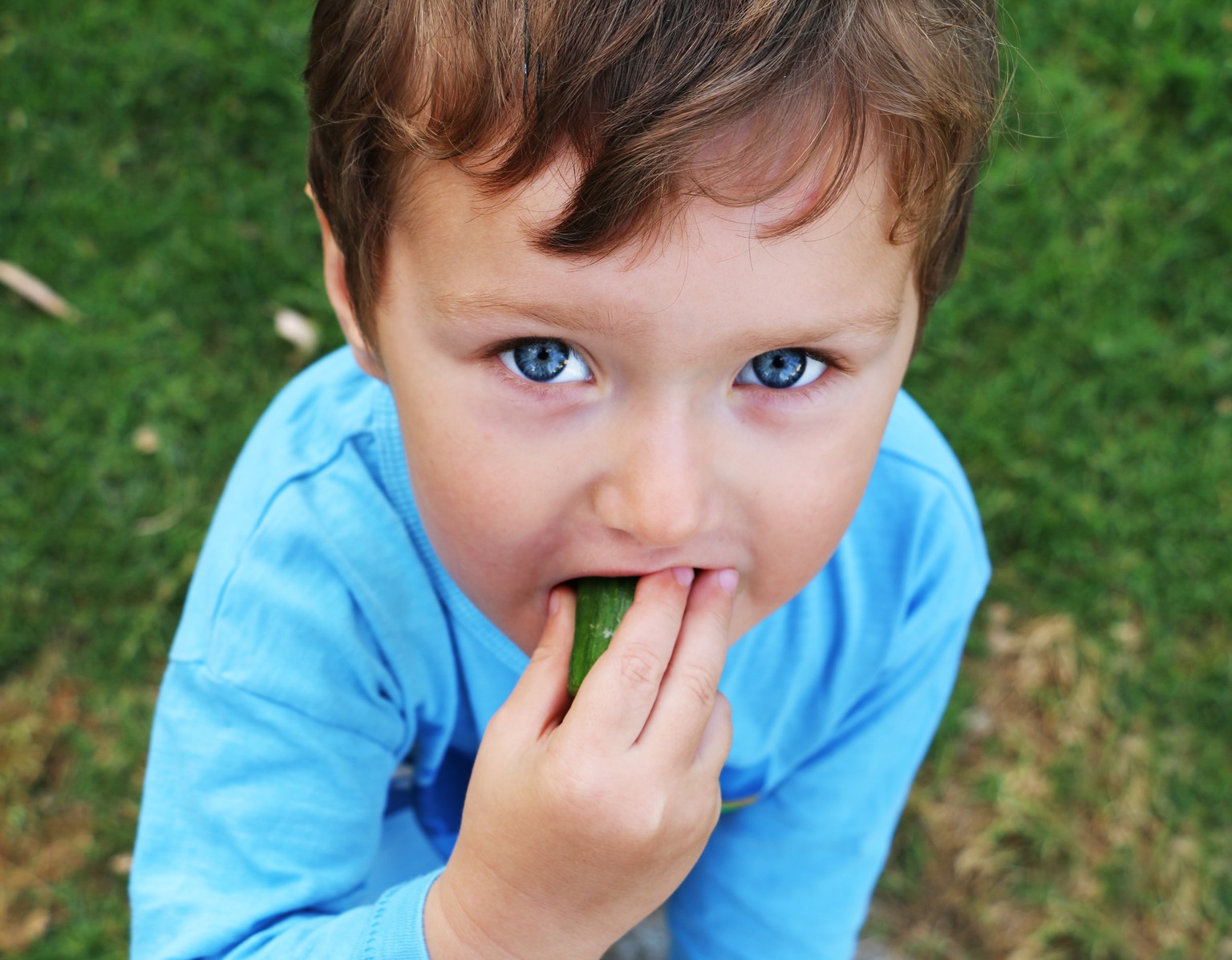 A little boy is eating a cucumber