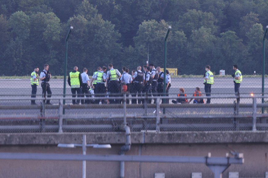 13.07.2023, Nordrhein-Westfalen, D�sseldorf: Polizisten stehen auf dem Flugfeld und versuchen Aktivisten der Gruppe Letzte Generation vom Asphalt zu l�sen, nachdem sie sich festgeklebt haben. Foto: Da ...
