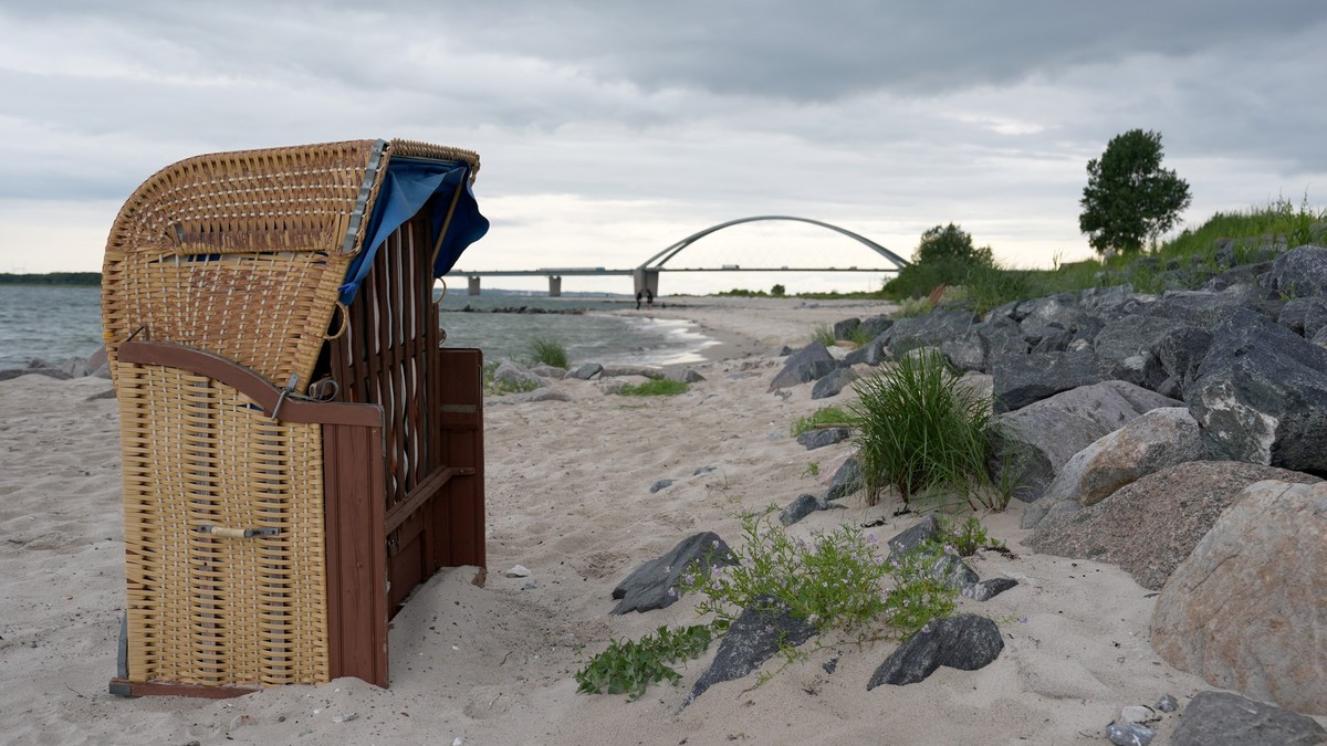 PRODUKTION - 03.07.2024, Schleswig-Holstein, Fehmarn: Ein Strandkorb steht unweit der Fehmarnsundbrücke am Strand. Zu Beginn der Hauptferienzeit sind in allen Regionen noch Übernachtungs- und Buchungs ...