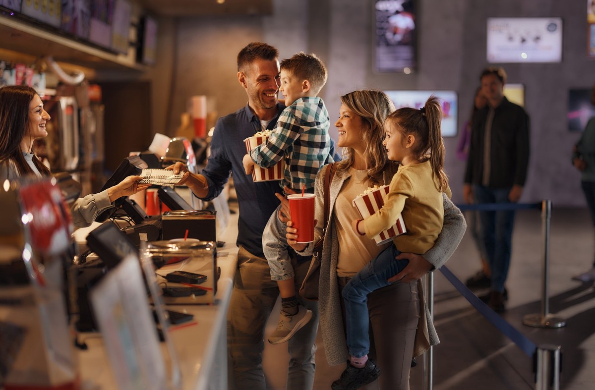 Happy parents and their kids buying movie tickets at concession stand in cinema.