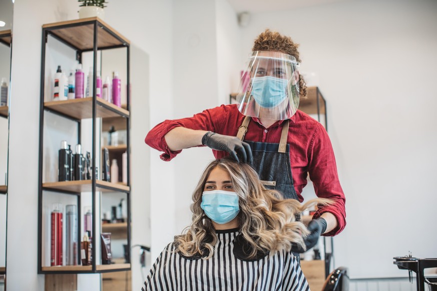 Young woman have hair cutting at hair stylist during pandemic isolation, they both wear protective equipment