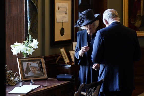 13.09.2022, Nordirland, Hillsborough: Königin Camilla hält einen Füllfederhalter, während sich König Charles III. Tinte von der Hand wischt. Der Monarch wollte sich in Hillsborough Castle in ein Gäste ...
