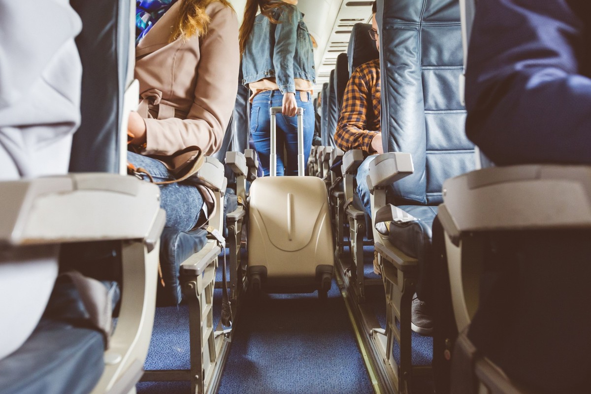 Interior of airplane with people sitting on seats. Passengers with suitcase in aisle looking for seat during flight.