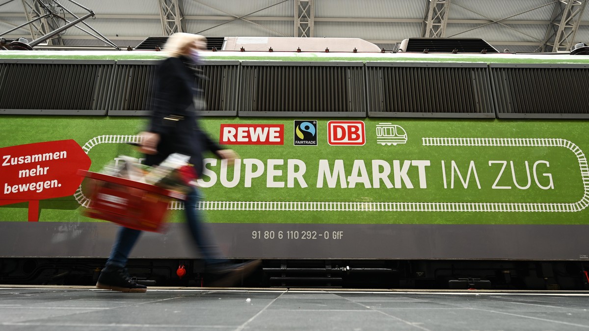 ILLUSTRATION - Eine Frau geht bei der Vorstellung des temporären Projekts "Fairer Supermarkt im Zug" im Frankfurter Hauptbahnhof an der Lok mit der Aufschrift "Dein Supermarkt im Zug&qu ...