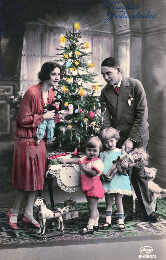 Greeting card features a colorized photograph of a family gathered around a small Christmas tree that sits on a low table, accompanied by the text &#039;Muchas Felicidades&#039; (translated from Spani ...