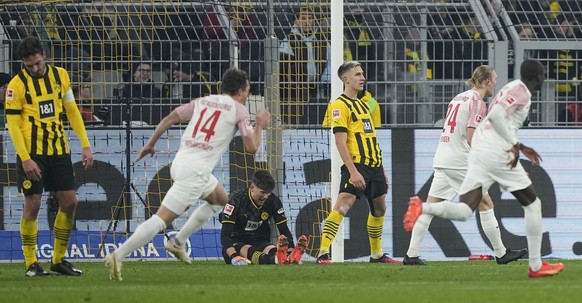 Dortmund's Mats Hummels, goalkeeper Gregor Kobel, and Nico Schlotterbeck, in black and yellow from left, show their dejection as Augsburg players run to celebrate after scoring their side's third goal ...